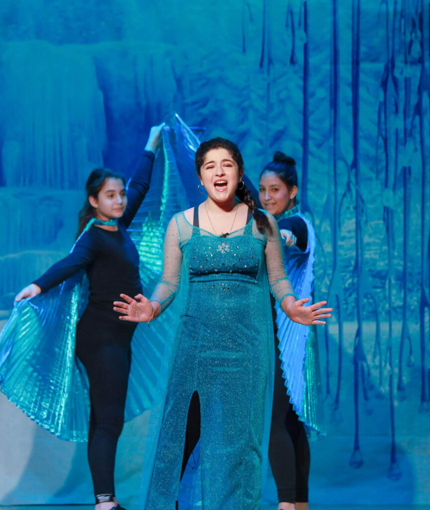 Girl playing Elsa on stage in The Frozen musical.