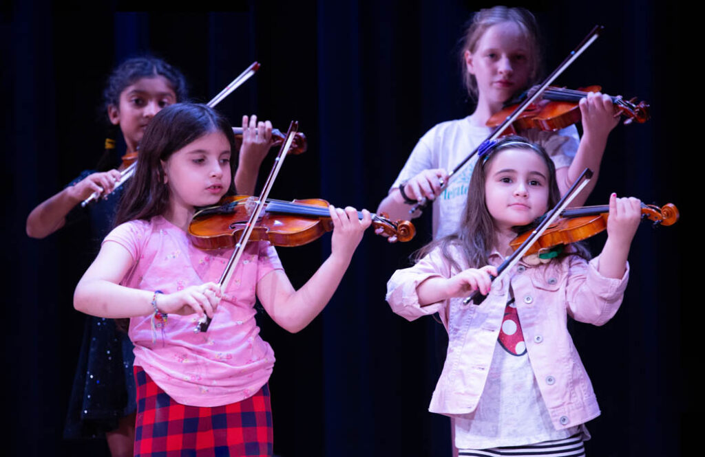Children playing the violin on stage.