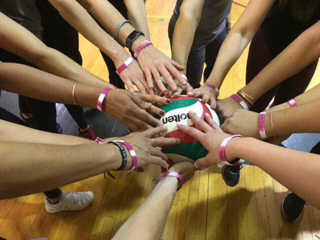 Team huddle with hands all touching a volleyball in the middle.