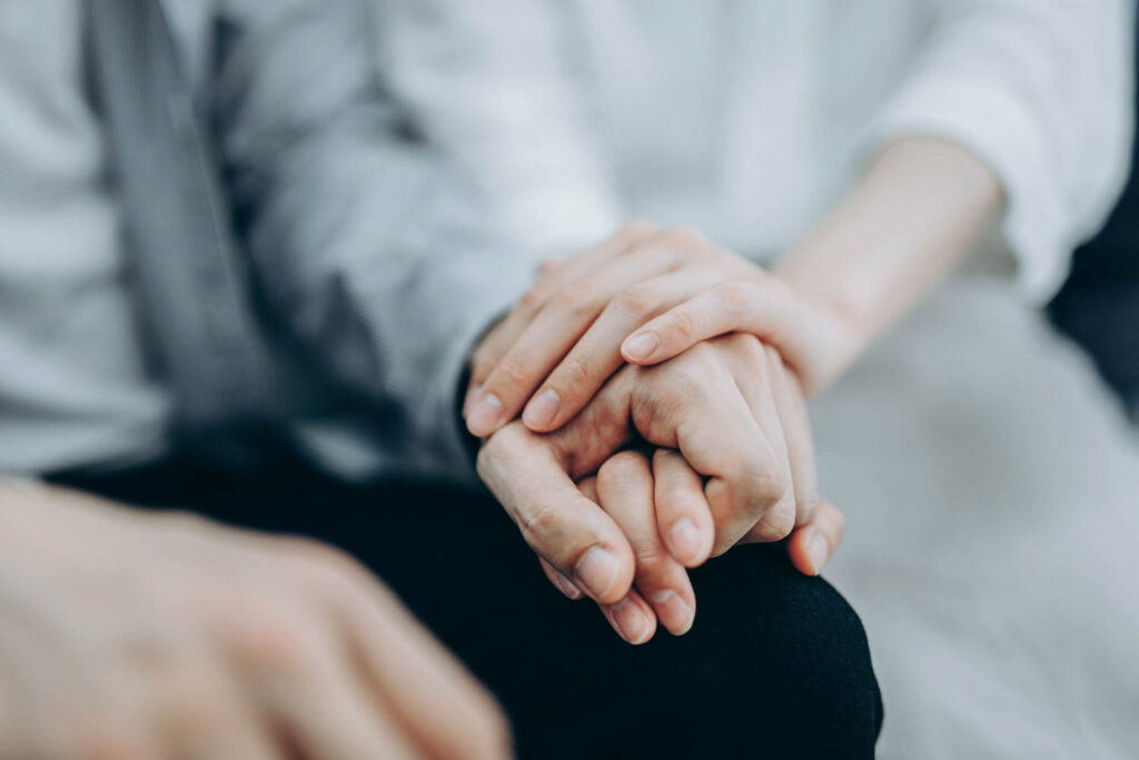 One person putting their hand on another persons hand in support group.