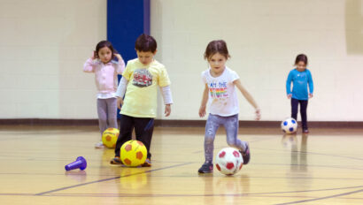 Kids playing soccer in a gym.