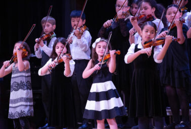 Children playing the violin on stage.