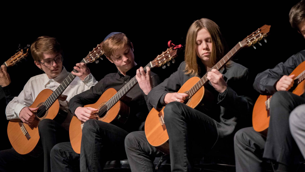 Teen boys playing all playing guitar on stage.