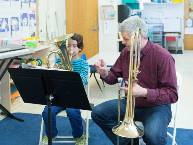 Teacher giving a horn lesson to a young boy.