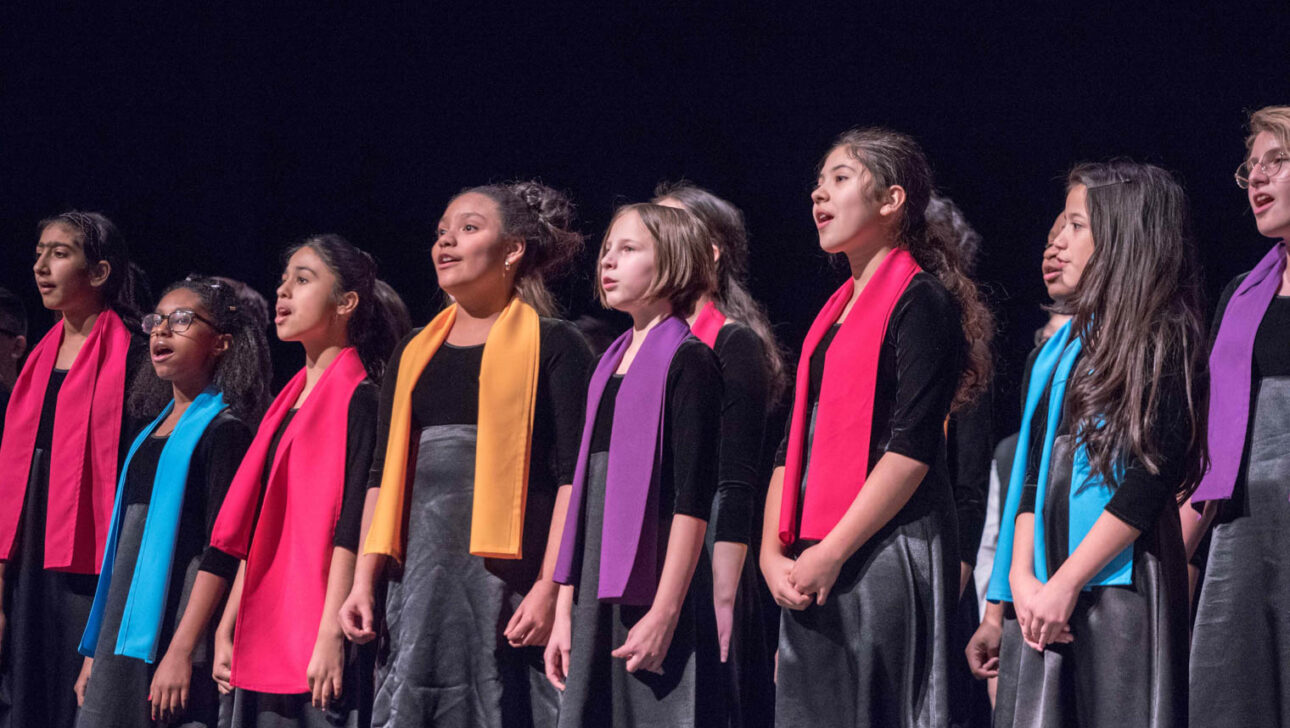 Girls in colored scarves singing on stage.