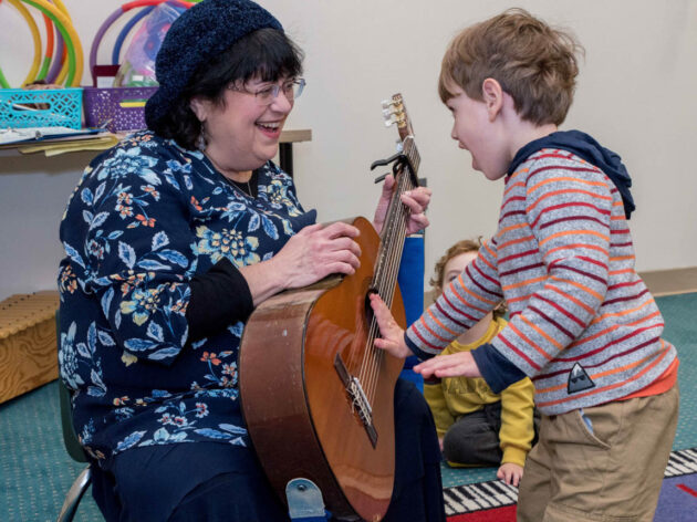 Teacher holding guitar while toddler touches it.