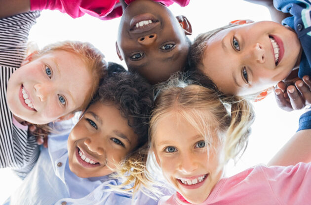 Kids in a group huddle smiling down at camera.