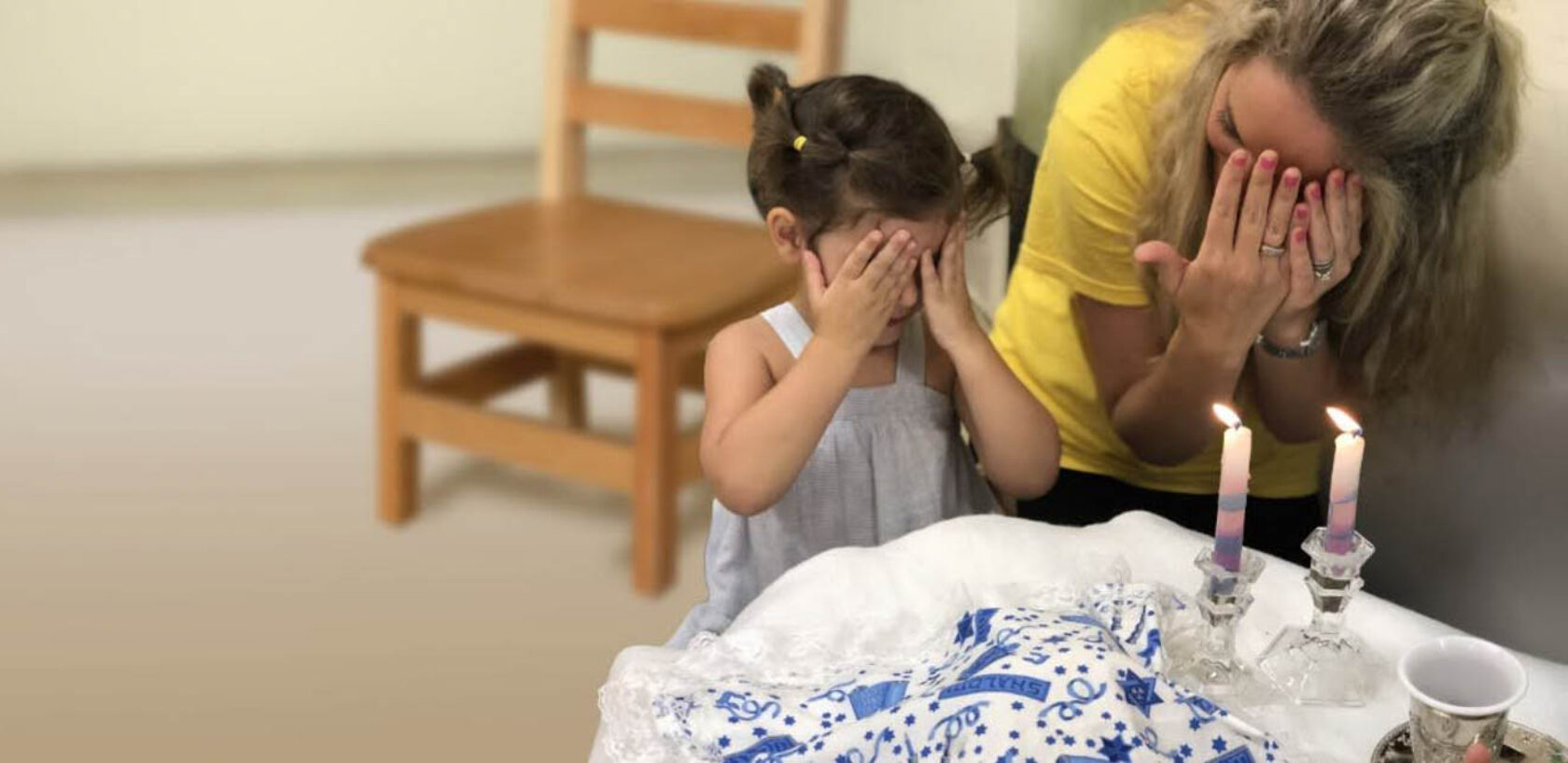 Woman and girl covering their eyes in front of a table with candles.